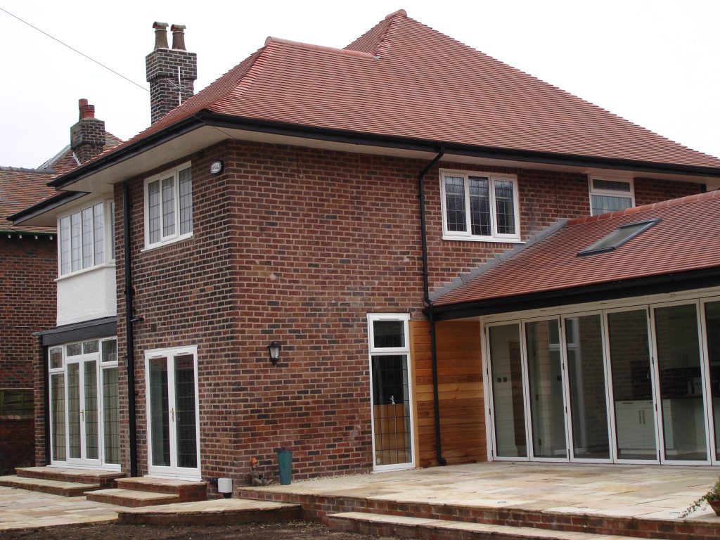 Completed rear of a brick house with new tiled roof, bi-folds and stone patio